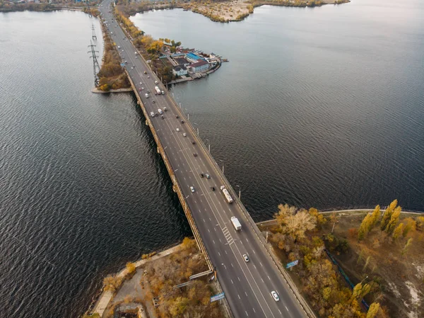 Воздушный панорамный вид на большую реку и транспортный мост через него с автомобилями осенью европейского города — стоковое фото