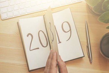 Kadın el üstten görünüm Not Defteri sayfası klavye ve kahve ile ahşap masa üzerinde çevirir. 2018 dönüyor, 2019 açma