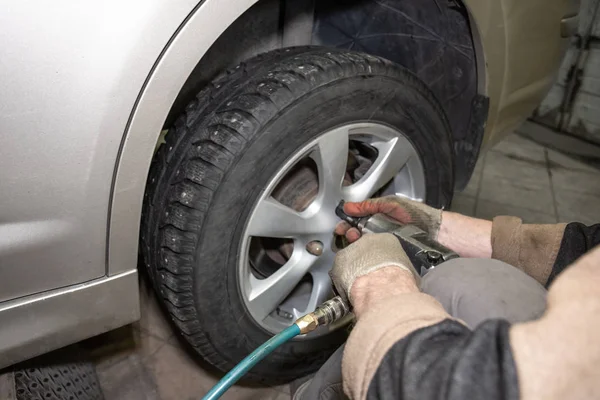 Car mechanic worker doing tire or wheel replacement with pneumatic wrench in garage of repair service station