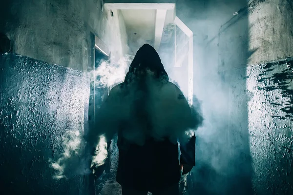 Dark silhouette of strange danger man in hood in back light with smoke or fog in scary grunge corridor or tunnel — Stock Photo, Image