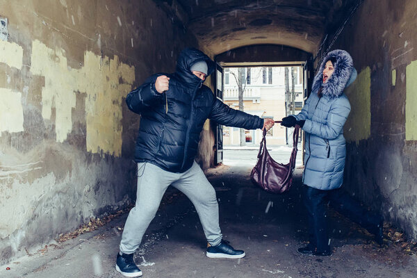 Robber with knife snatches bag from hands of woman. Criminal pickpocket and crimes on city street