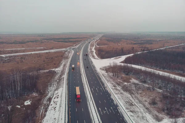 Aerial or top view from drone to winter asphalt highway or motorway road in countryside with cars and cargo logistic trucks traffic