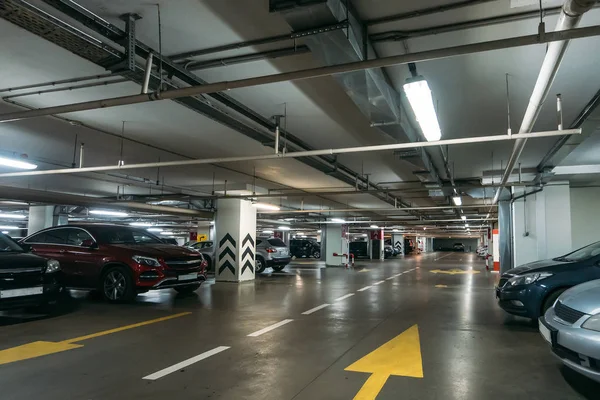 Parking souterrain éclairé intérieur sous le centre commercial moderne avec beaucoup de véhicules et des flèches sur le sol — Photo