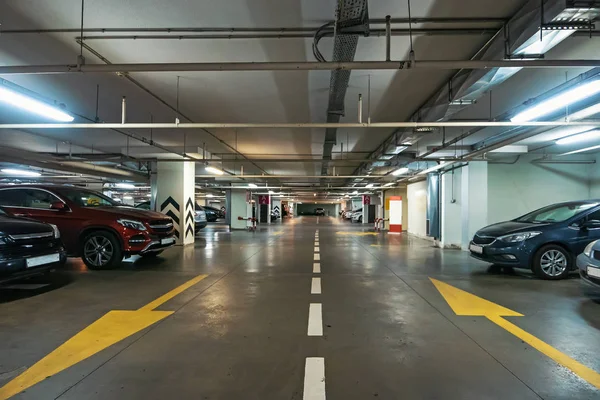 Teriluminasi parkir mobil bawah tanah interior di bawah mal modern dengan banyak kendaraan dan panah di lantai Stok Foto Bebas Royalti