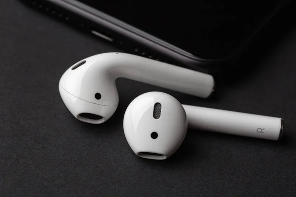 White wireless bluetooth earphones or headphones near smartphone on dark table, close up
