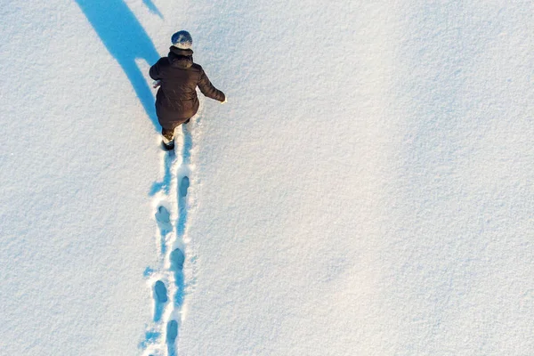 Menina caminha ou vai na neve deixando pegadas, vista aérea superior. Inverno atividade ao ar livre fundo com espaço de cópia — Fotografia de Stock