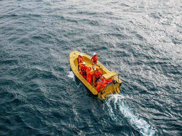 Kapal kuning industri dengan sekelompok pekerja yang tidak dikenal mengenakan seragam jingga di perairan samudera, pemandangan udara — Stok Foto