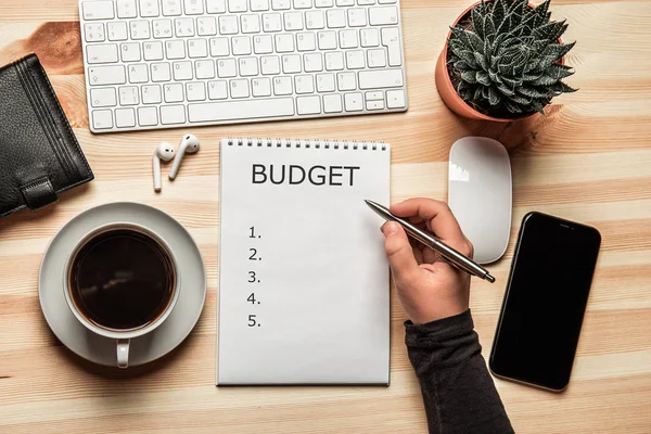 Költségvetési tervezés fogalma. A Jegyzettömb, a word költségvetés a munka asztal és a nő kezét toll felülnézet — Stock Fotó