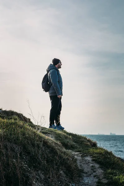 Üstünde tepe-in rock cliff çim ve deniz manzaraya, özgürlük macera kavramının arıyor adam Gezgin sırt çantası ile standları — Stok fotoğraf