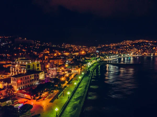 Vista aérea da noite aterro da cidade de Yalta com muitos edifícios e luzes refletidas na água do mar, tiro drone — Fotografia de Stock