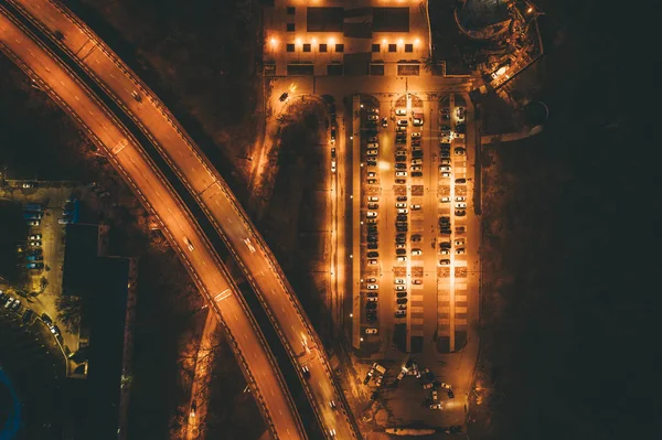 Luchtfoto bovenaanzicht van verlichte stad parkeerplaats met voertuigen 's nachts in de buurt van autosnelweg met verkeer — Stockfoto