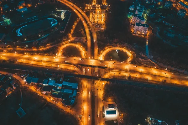 Flight on drone above night city with transport junction, asphalt city roads and Interchanges, aerial view of circle motorways with bridges and car traffic at night