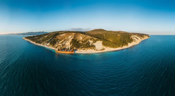 Aerial panorama of tropical island in sea or ocean and cargo ship run aground at coastline or sandy beach, drone photo from above view, copy space