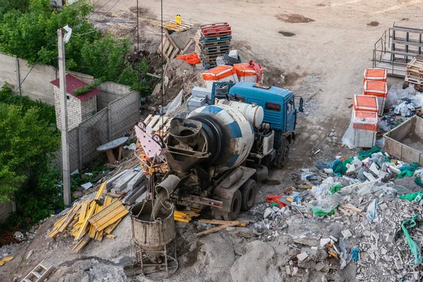 Concrete mixer machine pours liquid concrete into tank to be lifted onto roof by construction crane