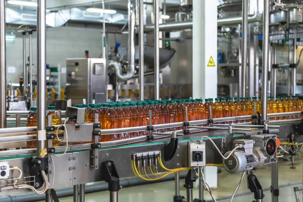 Botellas de plástico con jugo orgánico fresco en cinta transportadora automática o línea en la fábrica de bebidas o en el interior de la planta —  Fotos de Stock