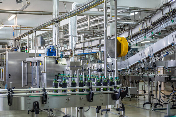 Conveyor belt or line in beverage plant with modern automated industrial machine equipment. Plastic PET bottles with fresh organic juice in factory interior