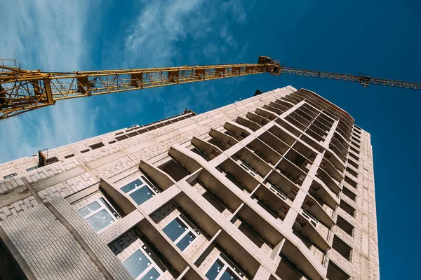 Промышленный кран на строительной площадке нового современного жилого здания на голубом фоне неба — стоковое фото