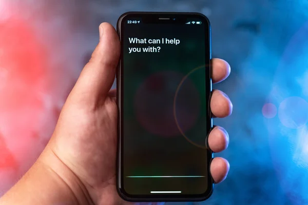 Moscou, Russie - Vers août 2019 : Siri - Assistant vocal numérique Apple activé par la voix dans la main des hommes et le texte sur l'écran de l'iPhone : Que puis-je vous aider ? Mode vocal d'interaction avec le téléphone — Photo