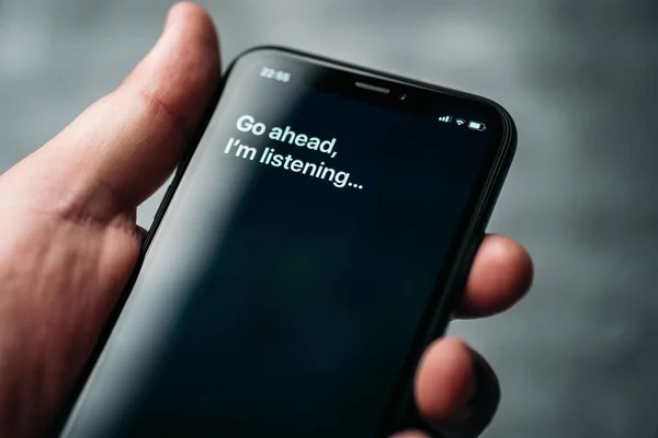 Moskow, Rusia - Sekitar Agustus 2019: Iphone XR di tangan laki-laki dan diaktifkan oleh asisten digital Apple suara Siri dan teks di layar telepon pintar: Silakan, saya mendengarkan Stok Lukisan  
