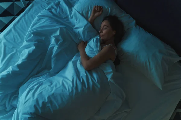 Ung vacker flicka eller kvinna sover ensam i stor säng på natten, uppifrån, blå tonas — Stockfoto