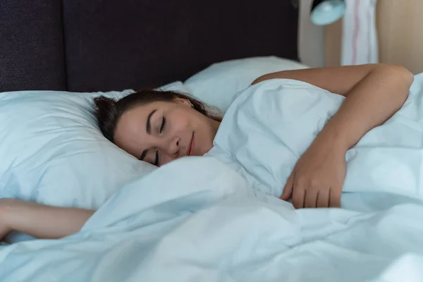 Ung vacker flicka eller kvinna sover ensam i stor säng på natten — Stockfoto