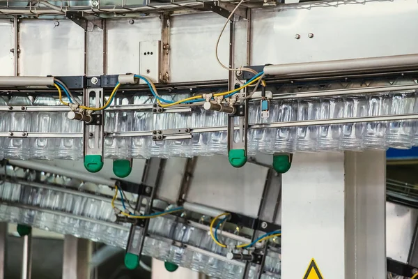 Botellas de plástico PET se mueven en la línea transportadora automática o cinta en la fábrica de agua o la producción de la planta, de cerca —  Fotos de Stock