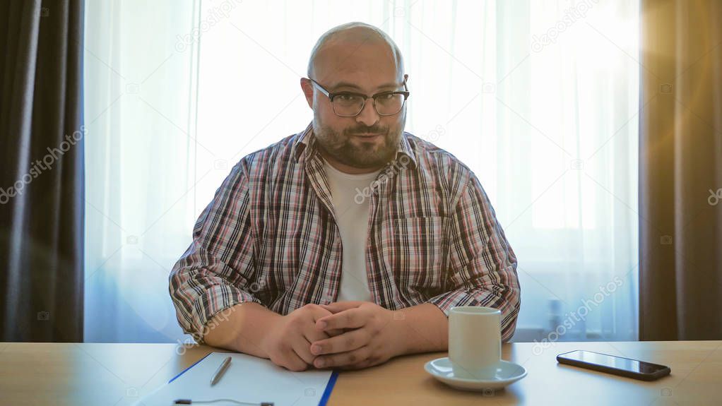 Male online teacher speaks on laptop webcam, fat man in glasses making videocall or webinar or job interview or talks with far friend via internet