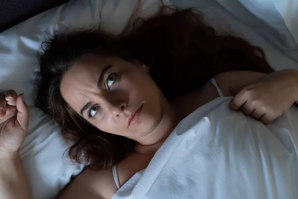 Depressed young woman dont sleep at night, lying on bed, looks up and suffers from insomnia, top view — Stock Photo, Image