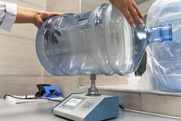 El trabajador comprueba el espesor de la botella de plástico o galón en el equipo de dispositivo especial. Planta de agua potable purificada, control de calidad —  Fotos de Stock