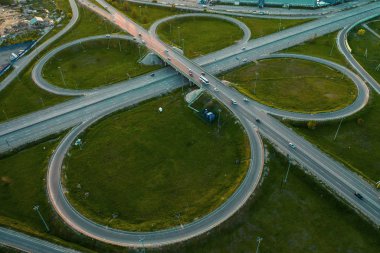 Gün batımında daire hareketi ile otoyol kavşağında veya yol kavşağında havadan görünüm, otomobil ve kamyon trafiği