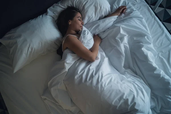 Ung vacker flicka eller kvinna sover ensam i stor säng på natten, uppifrån — Stockfoto