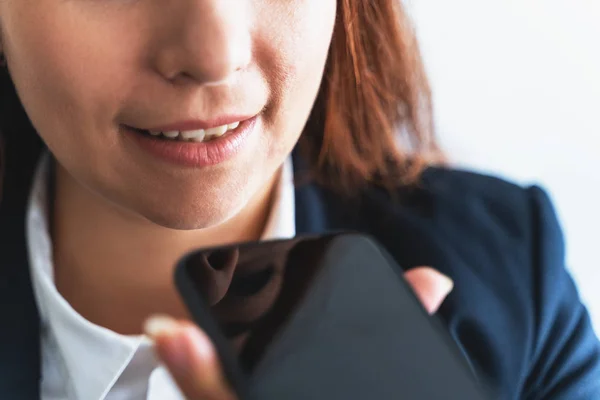 Jeune femme d'affaires souriante utilisant assistant vocal ou vocal numérique activé dans le smartphone, gros plan — Photo