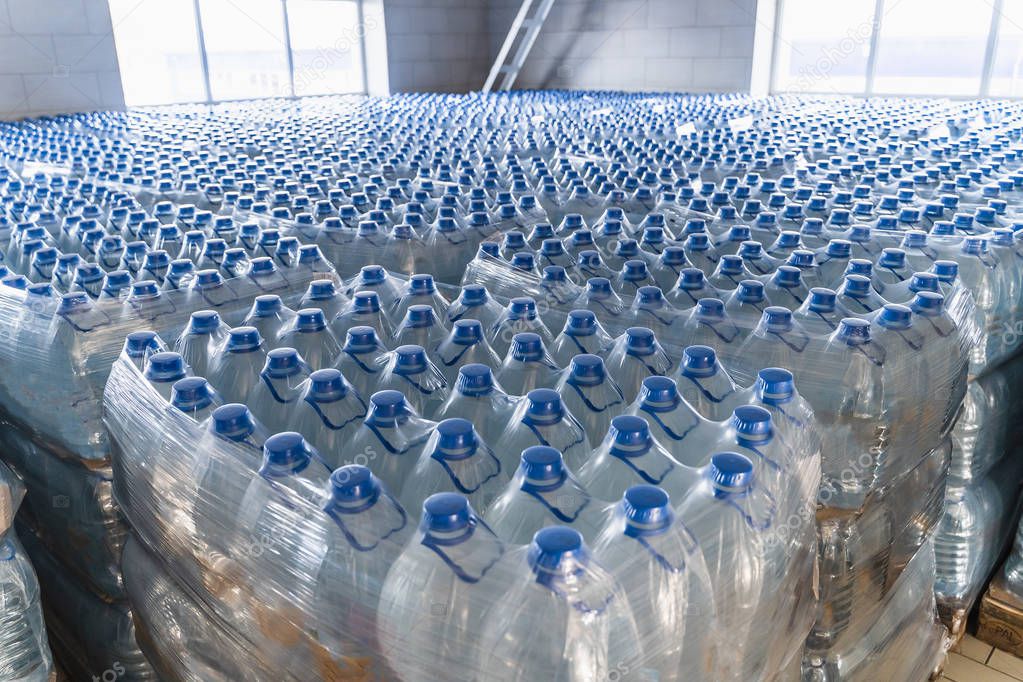 Many plastic bottles with drinking pure water and blue caps. Goods in factory warehouse or storehouse ready for delivery to supermarkets