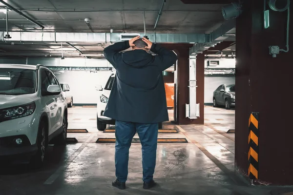 Stolen car concept. Surprised man discovered loss of car in underground garage parking lot, holding his head by hands