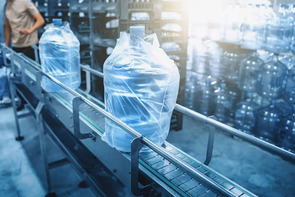 Conveyor line or belt with clean pure drinking water in plastic bottles packed in cellophane, loading finished goods at water factory, blue toned — Stock Photo, Image
