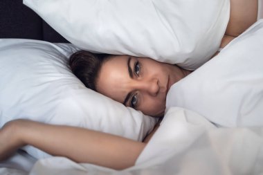 Genç stresli kadın uyuyamıyor ve başını ve kulaklarını yastıkla örtüyor.
