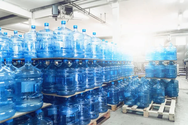 Gallons or plastic bottles of purified drinking water on pallets in water production factory interior inside in sunlight