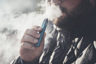 Adam yeni Vape Pod Sistemi içiyor, nefes alıyor ve nefes veriyor elektronik sigara buharı, buhar konsepti