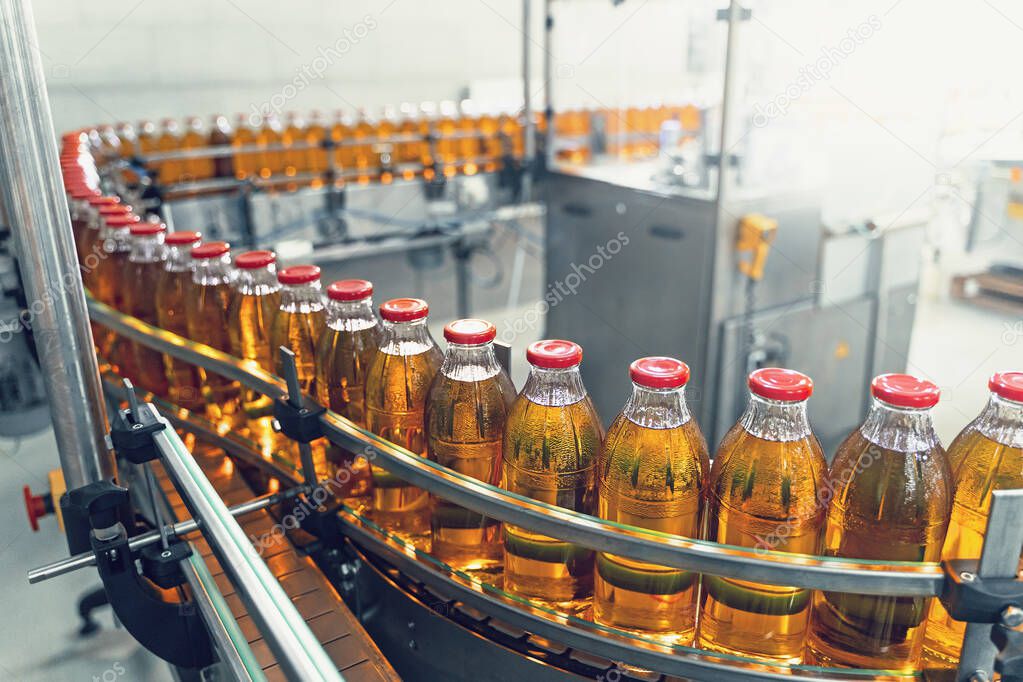 Conveyor belt, juice in glass bottles on beverage plant or factory interior, industrial manufacturing production line