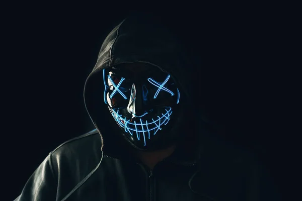 Uomo con illuminazione neon maschera bagliore in cappuccio su sfondo nero. Halloween e concetto di orrore — Foto Stock