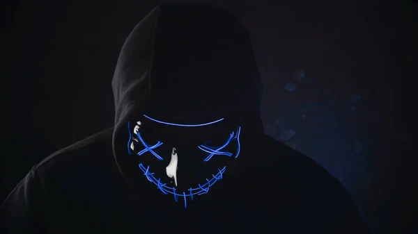 Uomo con illuminazione neon maschera bagliore in cappuccio su sfondo nero. Halloween e concetto di orrore — Foto Stock