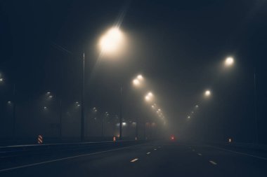 Gece sisli cadde ya da ıslak asfalt yol ve şehrin aydınlatması sonbahar sisi, korku atmosferi