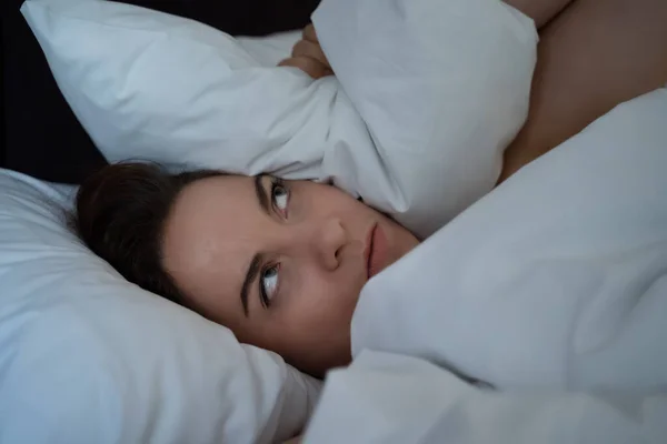 Young woman insomnia covered head with pillow, cant sleep from noise of neighbours, unhappy disturbed frustrated person at night — Stock Photo, Image