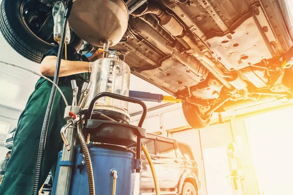 Pekerja menguras minyak dari mesin mobil selama pelayanan di Auto Service Station di bawah sinar matahari — Stok Foto