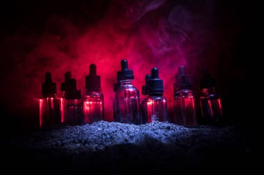 Vape konsepti. Karanlık arka planda duman bulutları ve tüp sıvısı şişeleri. Işık efektleri. Arka plan, vape reklamı ya da vape arkaplan olarak kullanışlı. Seçici odak