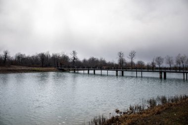 Bridge kış ağaç ve mavi bulutlu gökyüzü güneşli gün boyunca ile Orman Gölü. Arka plan ve fırtınalı bulutlar gökyüzü üzerinde orman ile güzel doğal dağ gölü. Azerbaycan doğa