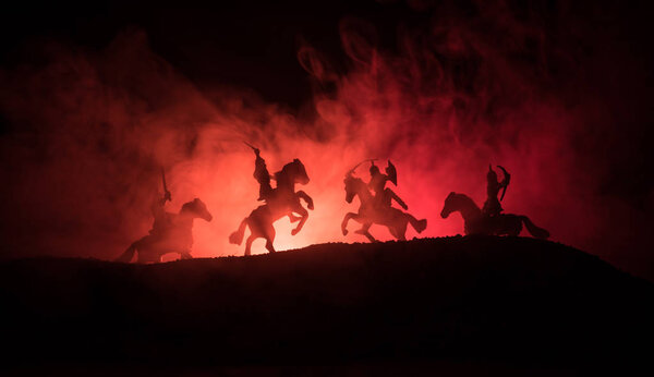 Medieval battle scene with cavalry and infantry. Silhouettes of figures as separate objects, fight between warriors on dark toned foggy background. Night scene. Selective focus