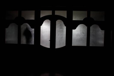 Kapalı cam bir kapıdan geçen, bilinmeyen bir gölge figürünün silueti. Geceleri pencerenin önündeki bir insanın silueti. Manyağın bulanık silueti korkunç cadılar bayramı konsepti.