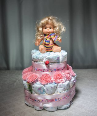 Yeni doğan Hediyelik konsepti. Bebek bezi kek. Çiçekli pasta olarak kaydırılan çocuk bezi. Tablo ile dekore edilmiş oyuncak bebek üzerinde kaydırılan temiz bebek bezi kek. Seçici odak.