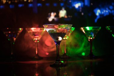 Ünlü kokteyl Martini, birkaç bardak koyu tonda sisli arka plan ve disko ışıkları ile bir barda vurdu. Club içki kavramı. Seçici odak